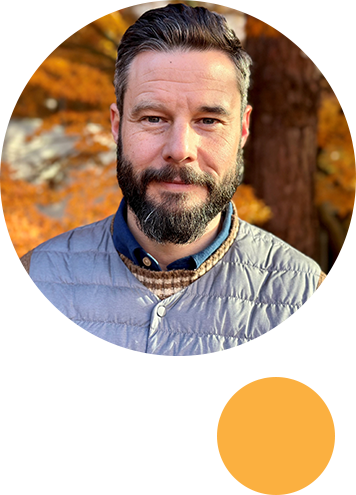 Photo of Dr. Valley with short dark hair and a beard looking directly at the camera. The background looks fall-like.